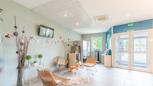 A modern reception area with wicker chairs, a white round table, and a large window. - Appart'City Classic Bordeaux Aéroport St Jean D'Illac (Saint-Jean-d'Illac)