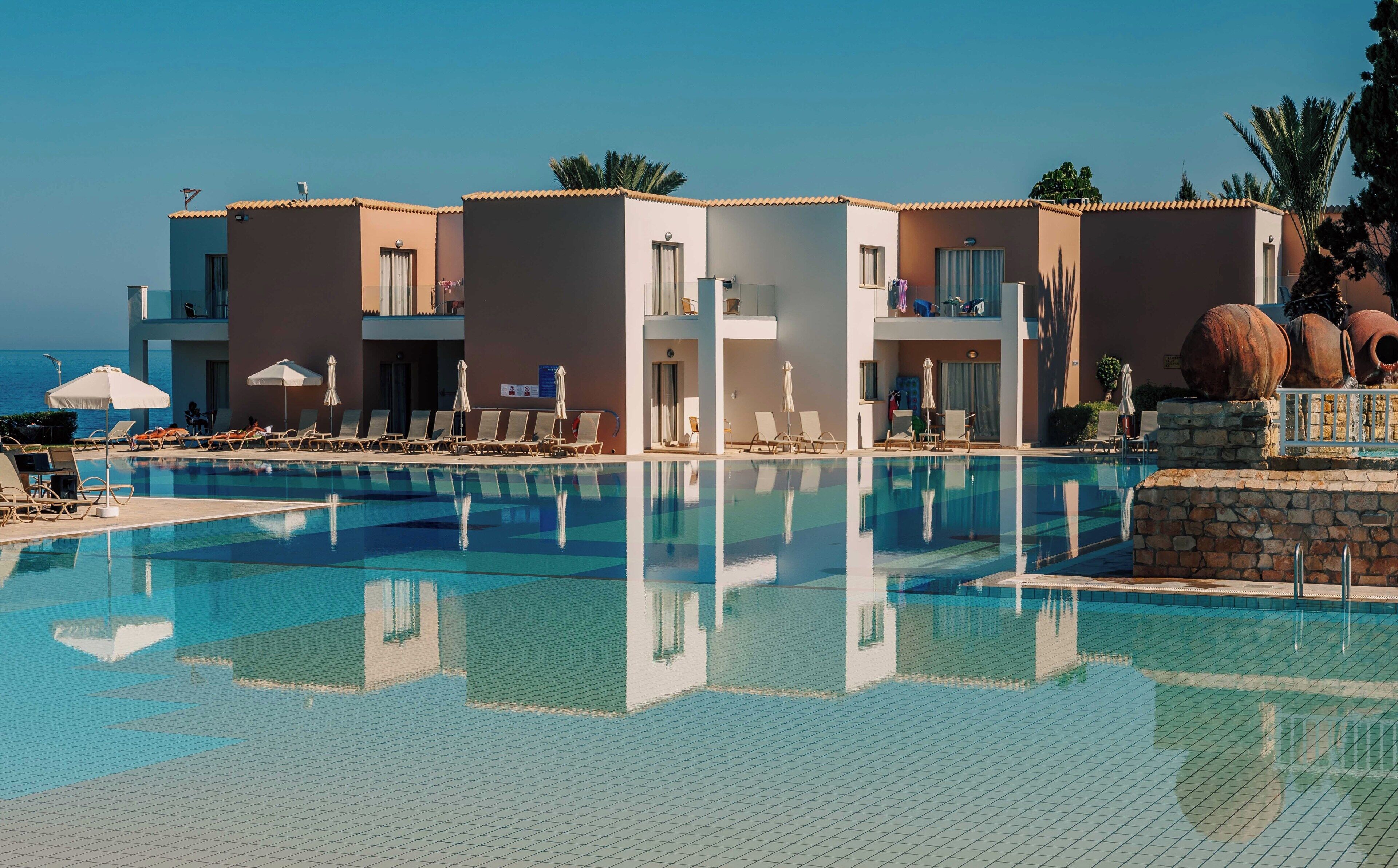 A hotel with a swimming pool, sun loungers, and a view of the sea.