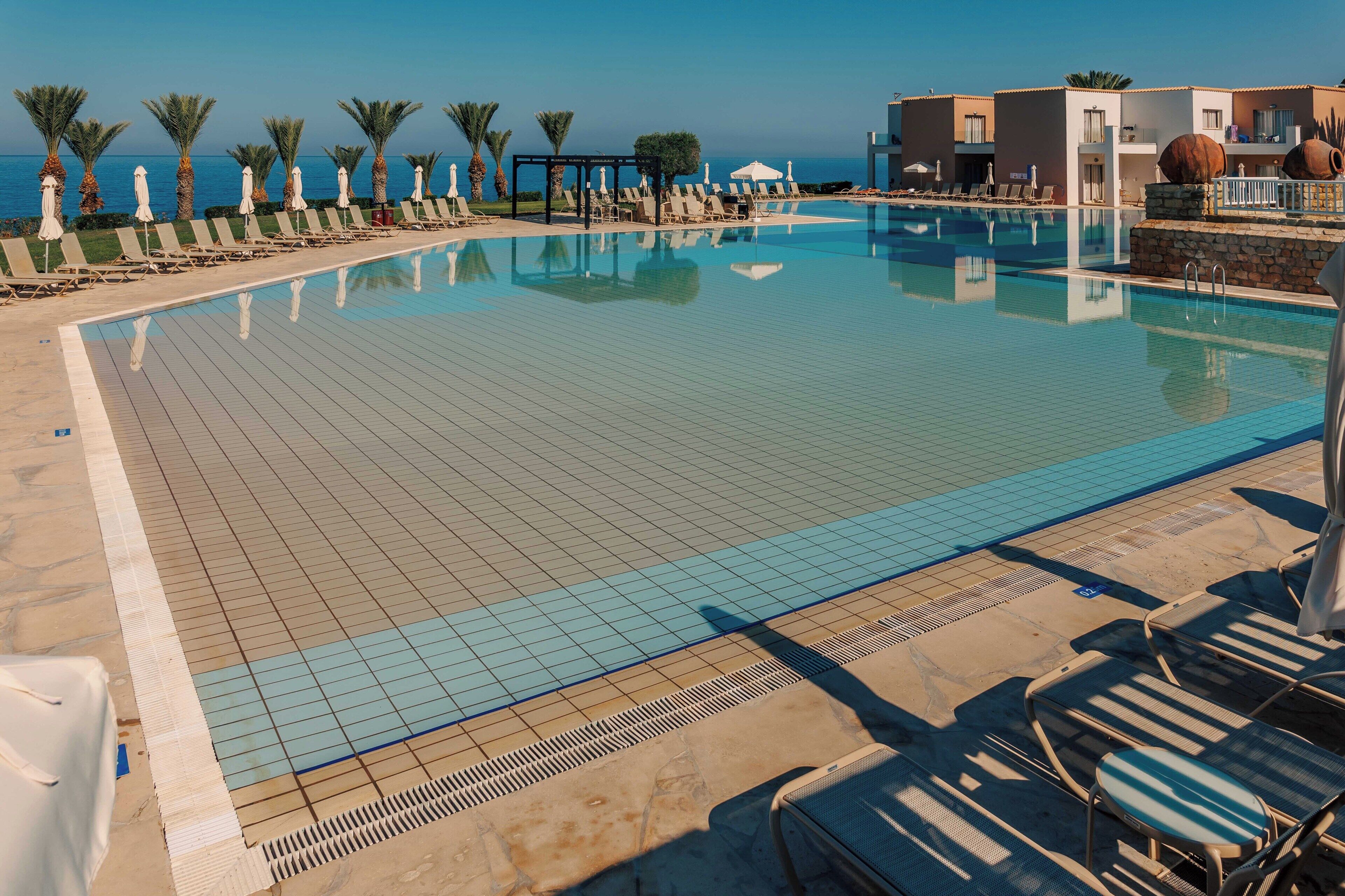 Uma piscina com espreguiçadeiras e guarda-sóis, céu claro e vista para o mar.