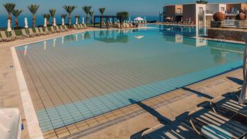 A swimming pool with lounge chairs and umbrellas, a clear sky, and a view of the sea.