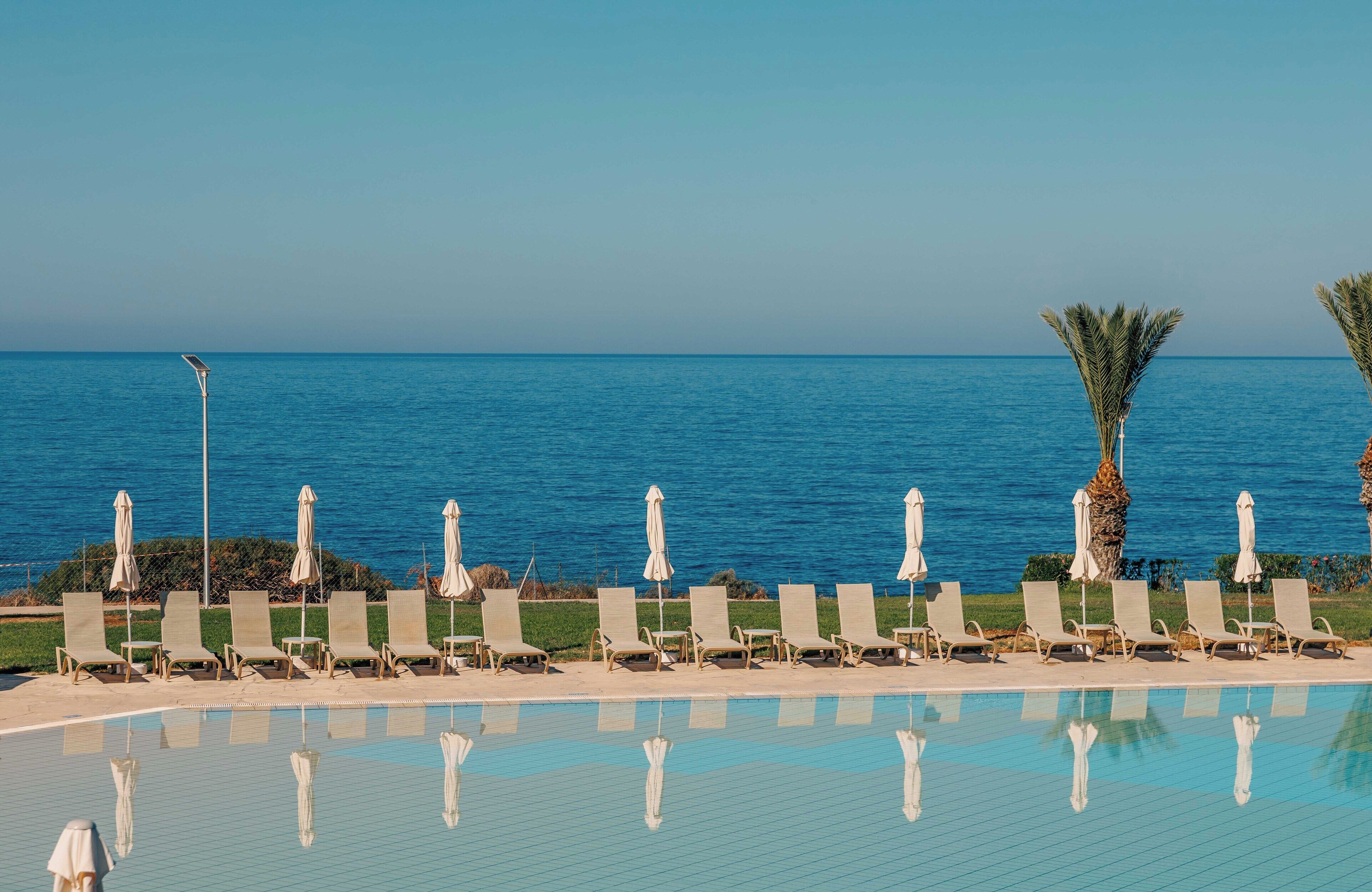 A poolside area with lounge chairs and umbrellas, overlooking a calm sea.