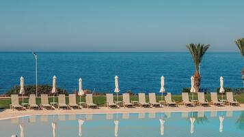 A poolside area with lounge chairs and umbrellas, overlooking a calm sea.