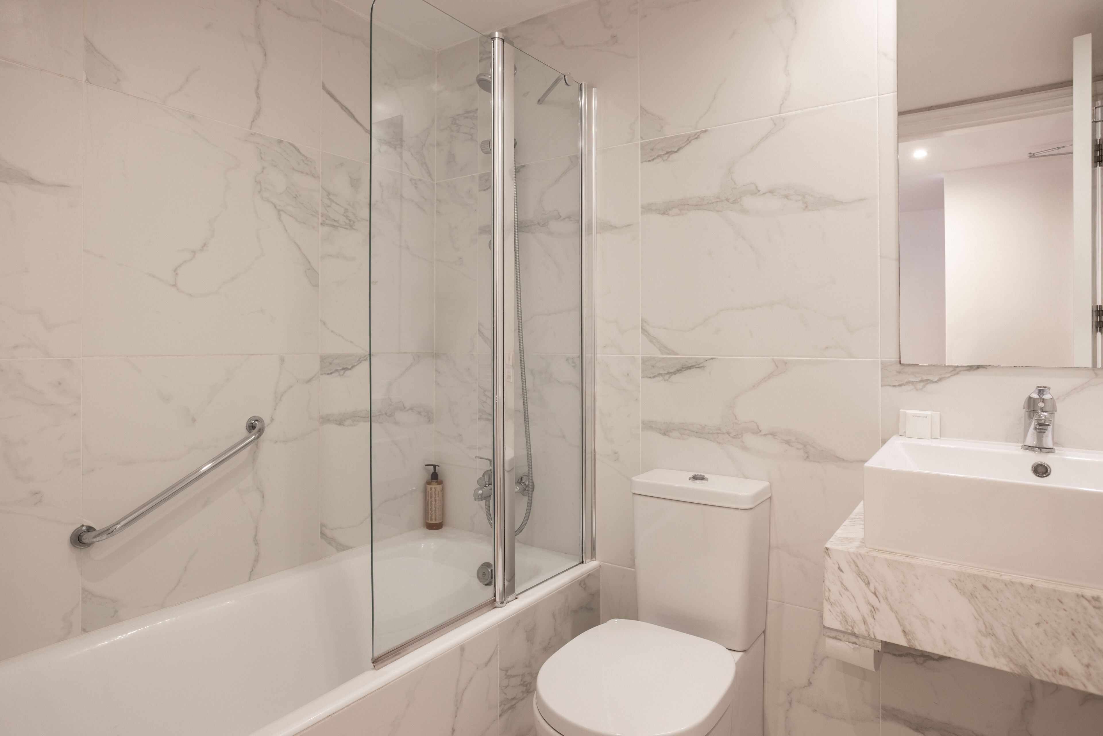 A modern bathroom with a glass-enclosed shower, a white toilet, and a marble-tiled sink area.