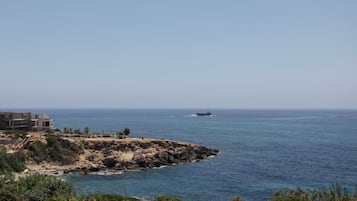 Vista costera con un edificio en la orilla rocosa y un barco a lo lejos.