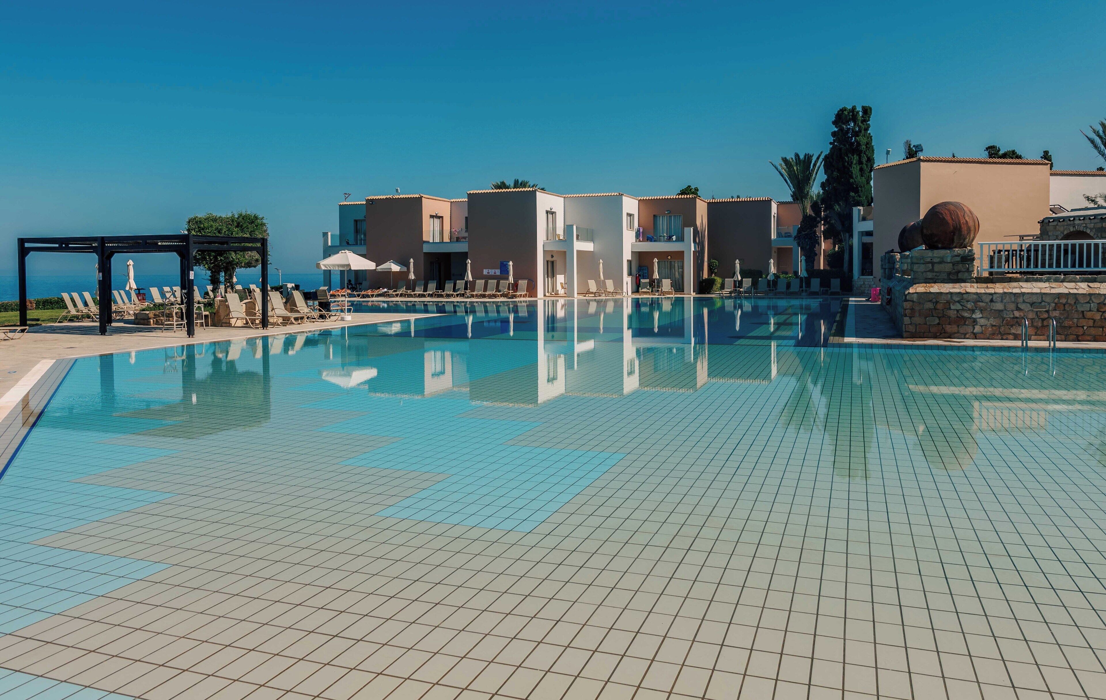 Une piscine avec un revêtement de sol en carrelage, des chaises longues et une vue sur la mer.