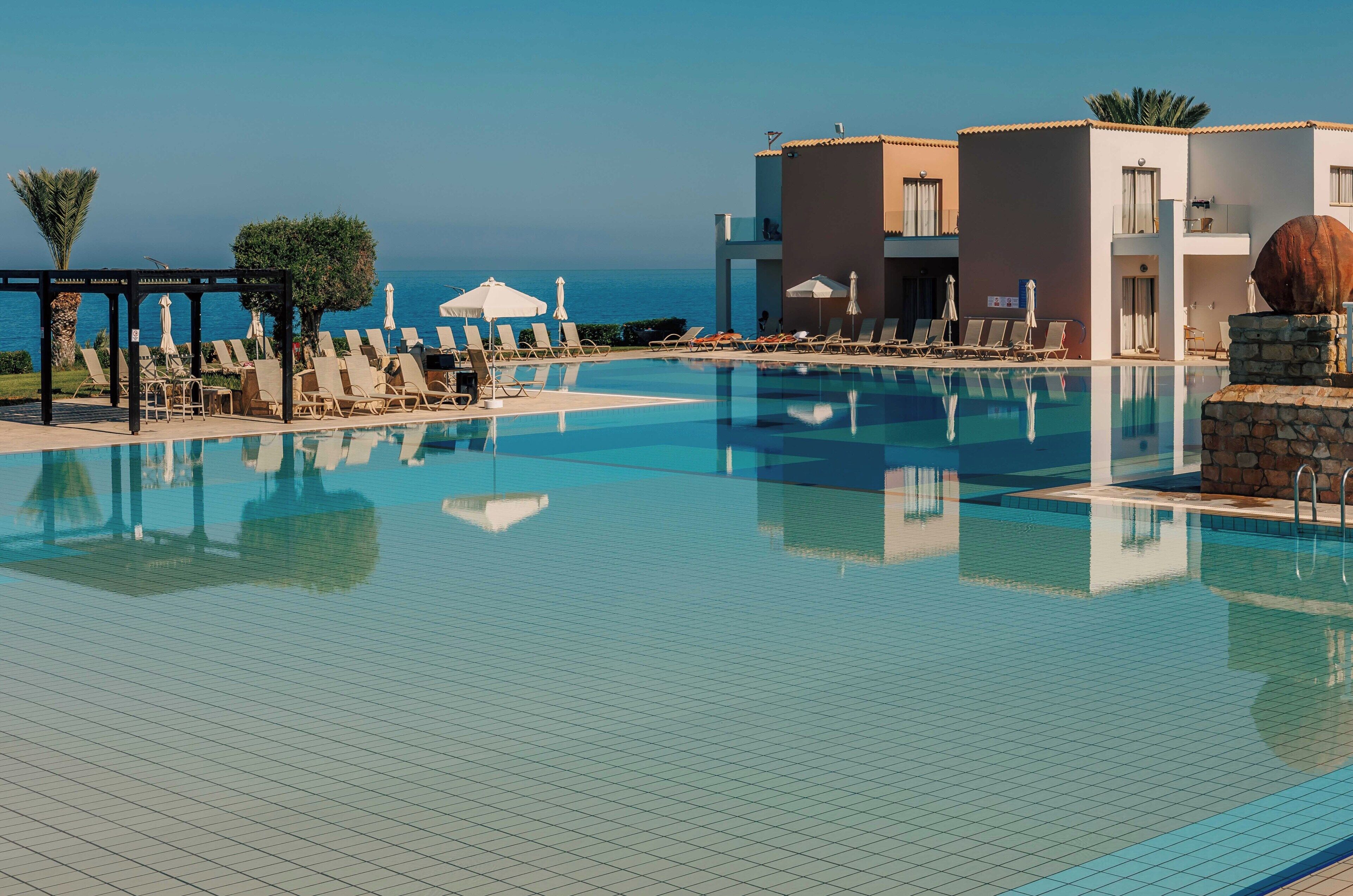 Un espace piscine avec des chaises longues et des parasols, un ciel dégagé et une vue sur la mer.