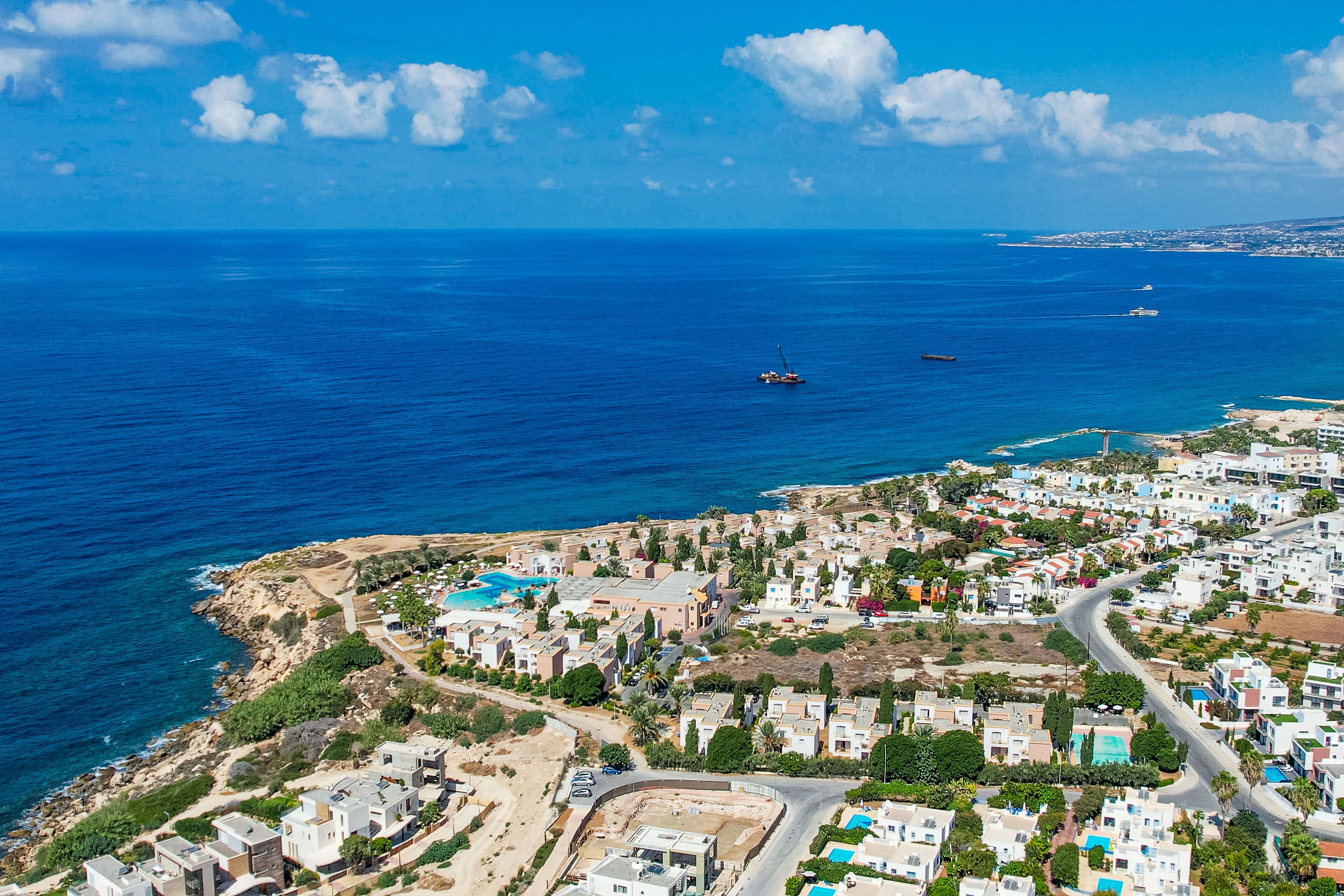 An aerial view of a coastal town with a clear blue sea, a small boat, and a mix of residential buildings.