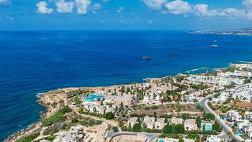 An aerial view of a coastal town with a clear blue sea, a small boat, and a mix of residential buildings.