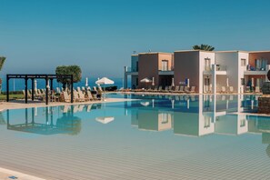A swimming pool with lounge chairs and umbrellas, a clear sky, and a building with balconies. - Atlantica Akteon (Chlorakas)