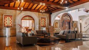 Un hall espacioso con sofás de cuero, una mesa de centro y un candelabro. Se observan ventanas de vitral y un letrero que indica 'Alamosa Restaurant'.