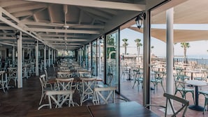 Un comedor interior con mesas y sillas, ventanas amplias y vista a la playa.