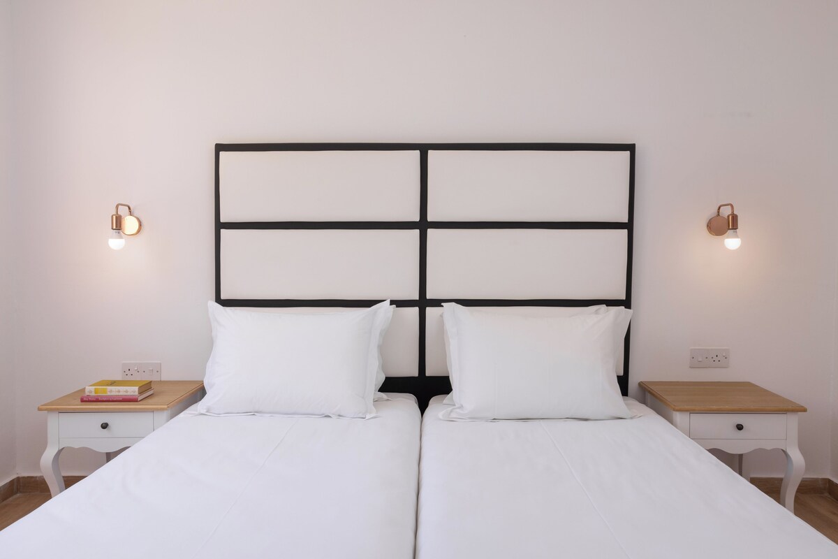 A double bed with a black and white headboard, two bedside tables with lamps, and a small bedside drawer.