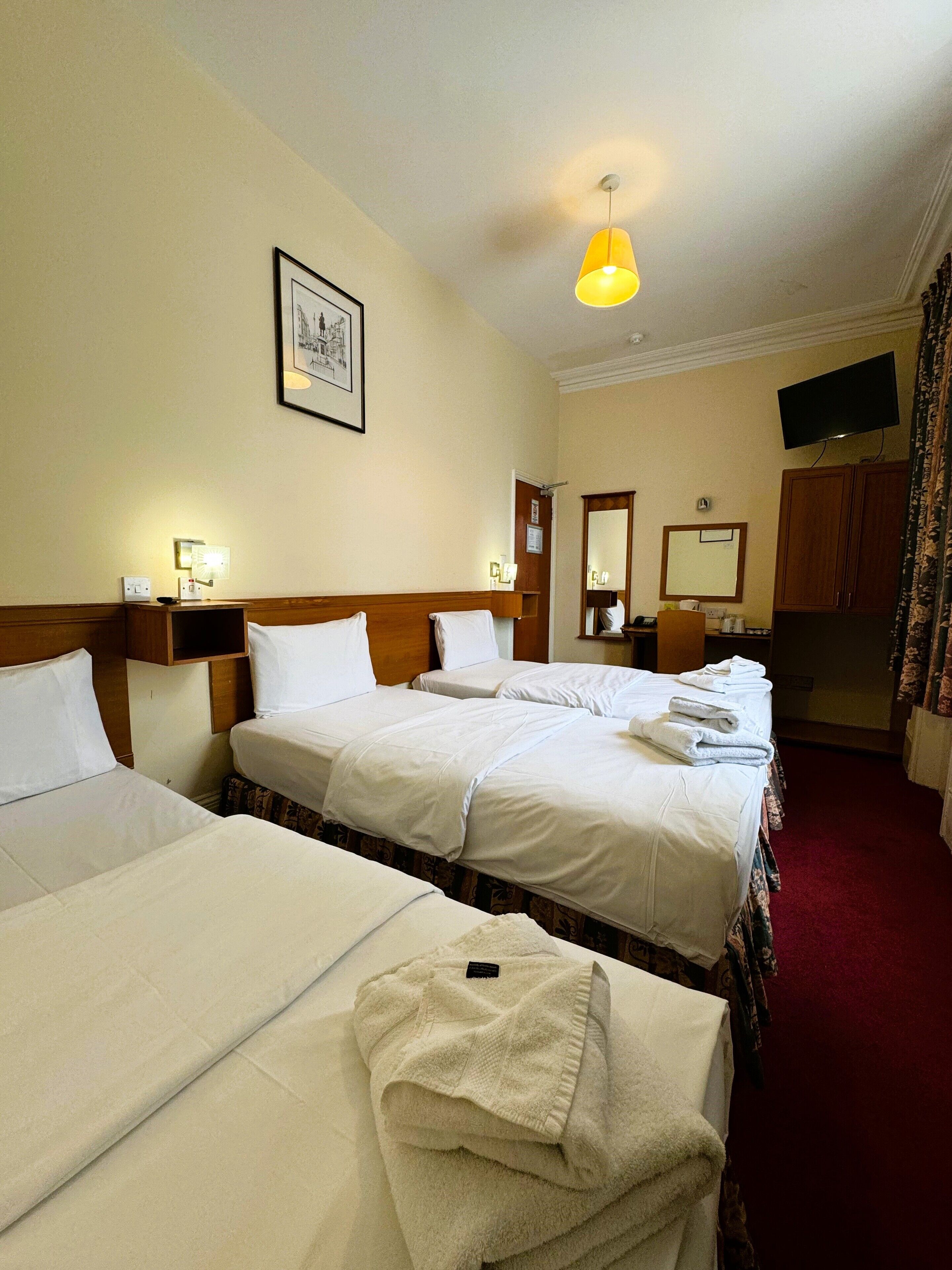 A hotel room with three beds, a television, a mirror, and a framed picture on the wall.