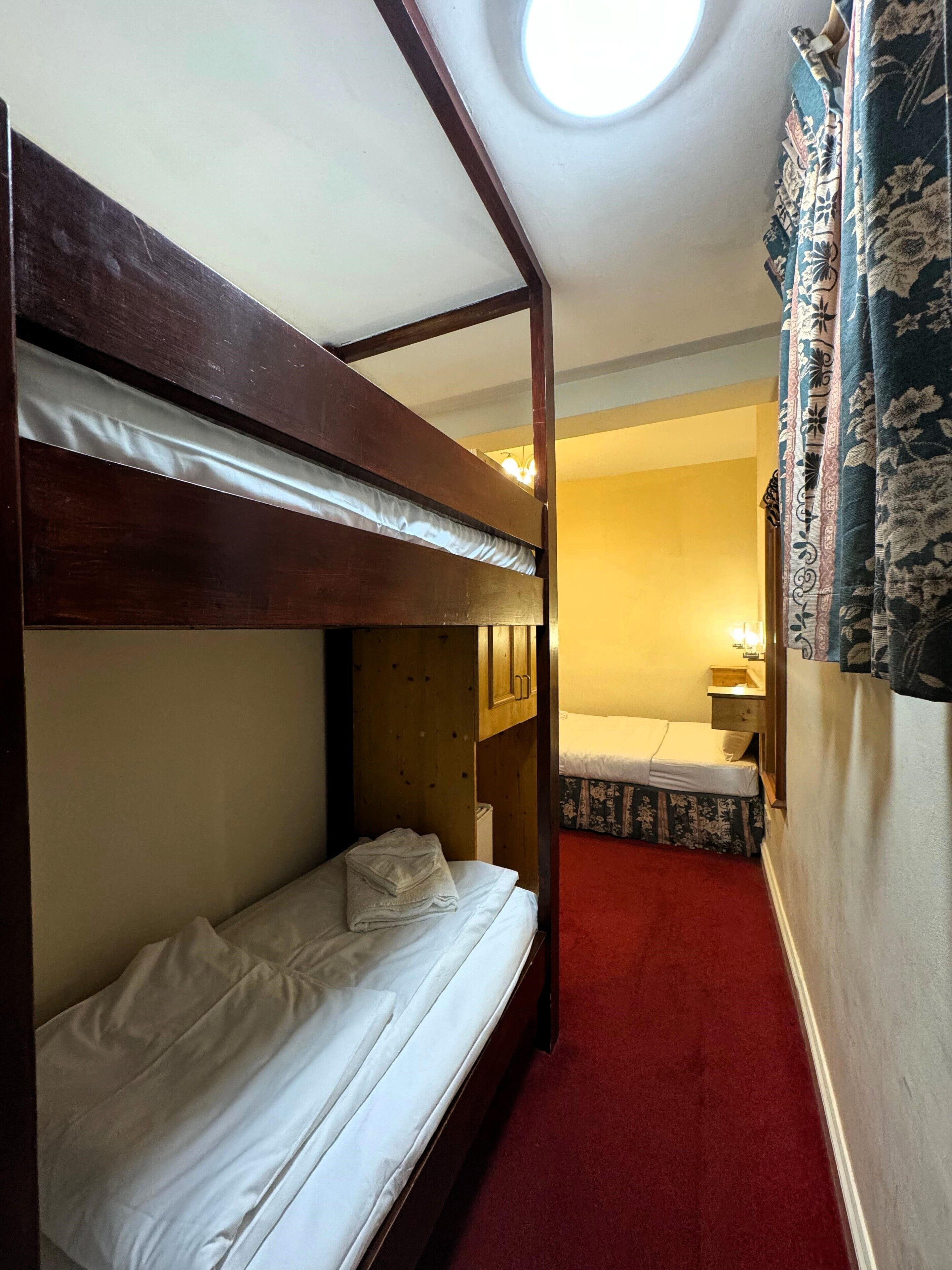A bunk bed room with a skylight, a small bedside table, and a red carpet.