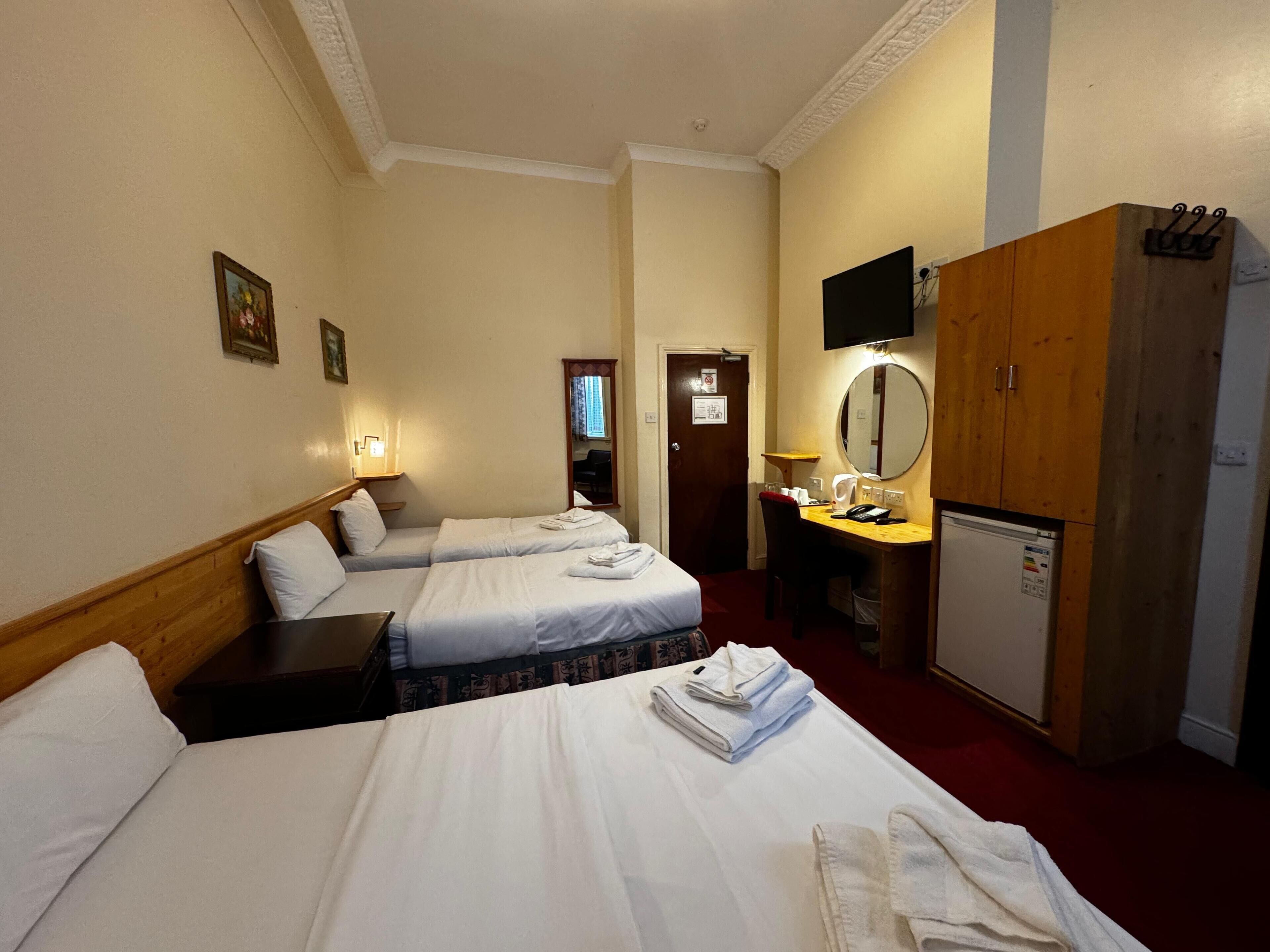 Ein Hotelzimmer mit zwei Betten, einem Schreibtisch mit Spiegel, einem Fernseher und einem Kleiderschrank.