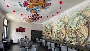 A conference room with tables and chairs, a mural of palm trees, and red lanterns on the ceiling. - Bridge Park Hotel (London)