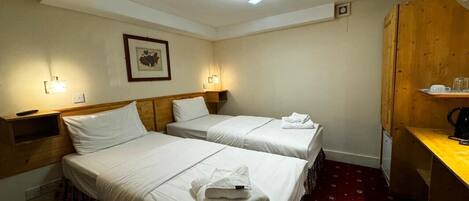 A hotel room with two beds, a wooden desk, and a red patterned carpet.