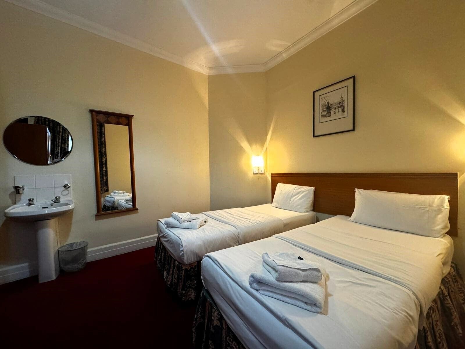 A hotel room with two beds, a sink, a mirror, and a framed picture on the wall.