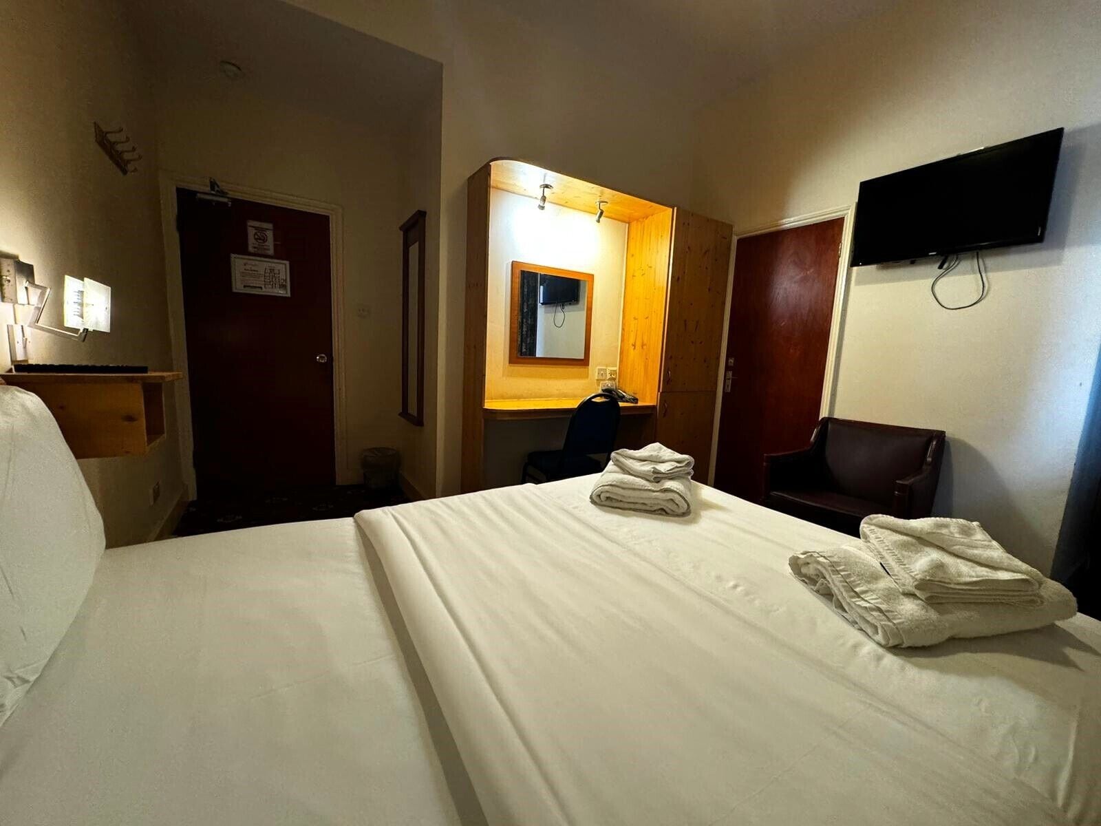 Hotellihuone, jossa on suuri sänky, työpöytä, tuoli, televisio ja peili.