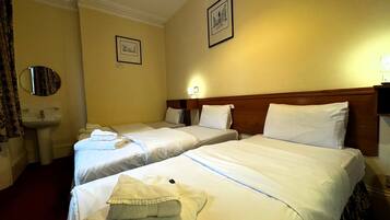 A hotel room with two single beds, a round mirror, a sink, and a framed picture on the wall.