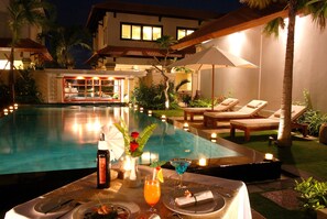 Un área de comedor junto a la piscina, con una mesa para dos, una botella de vino, una copa de martini y una vela.