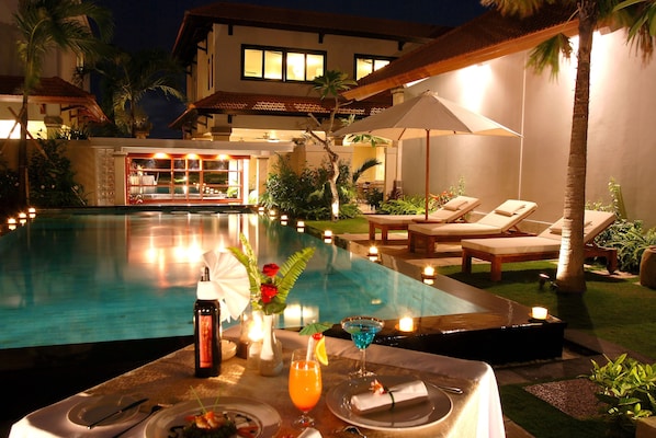 Un área de comedor junto a la piscina, con una mesa para dos, una botella de vino, una copa de martini y una vela.