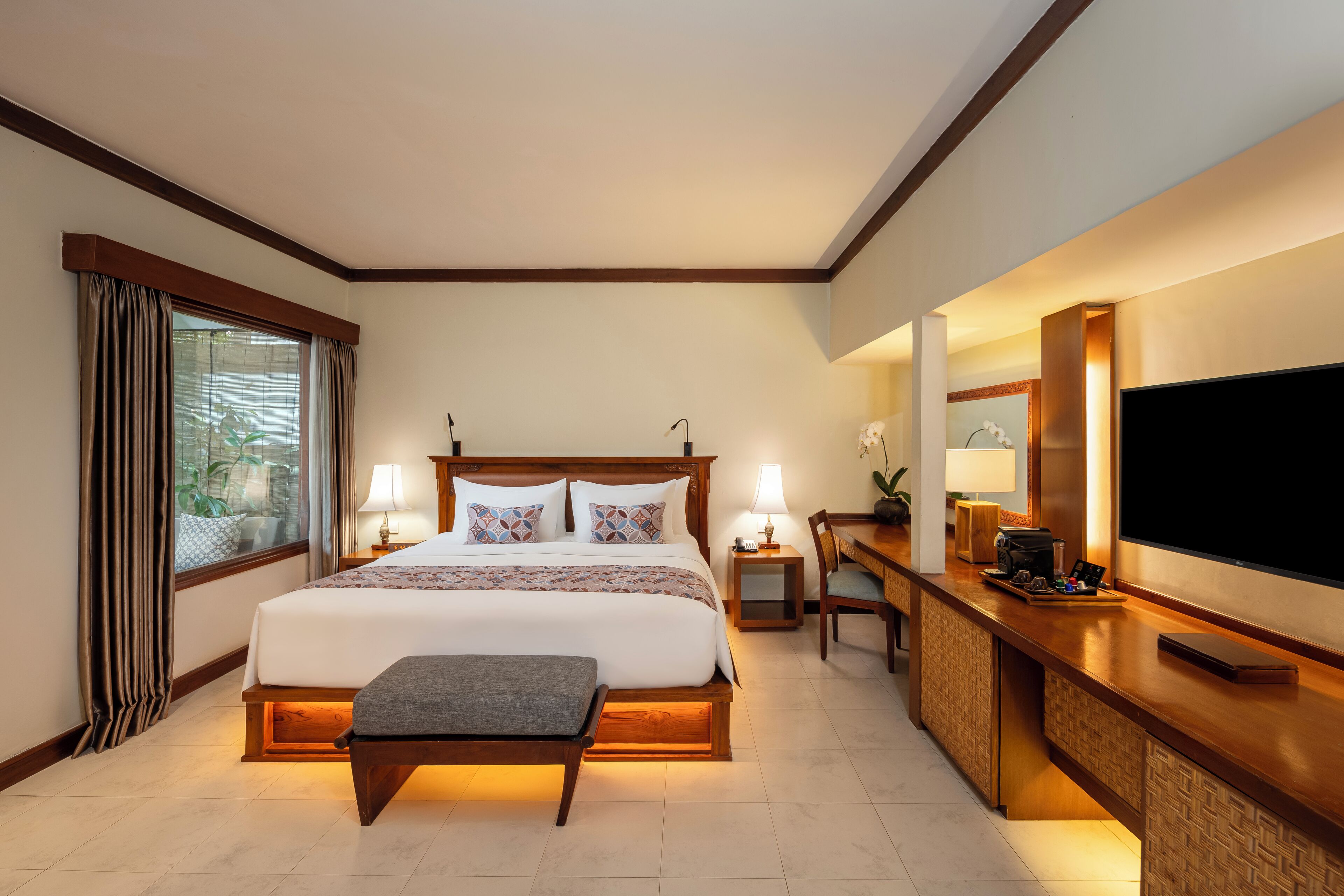 Une chambre d’hôtel avec un grand lit, des lampes de chevet, un bureau avec un téléviseur à écran plat et une fenêtre avec des rideaux.
