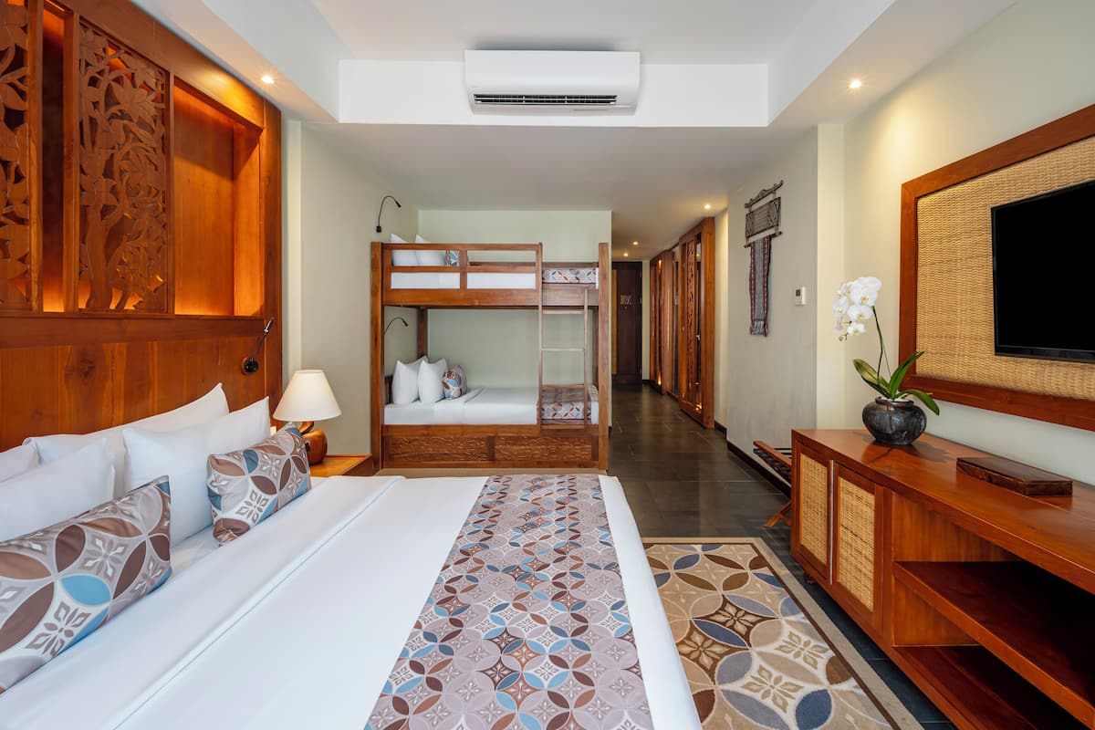 A hotel room with a large bed, a bunk bed, a TV, and a wooden cabinet.
