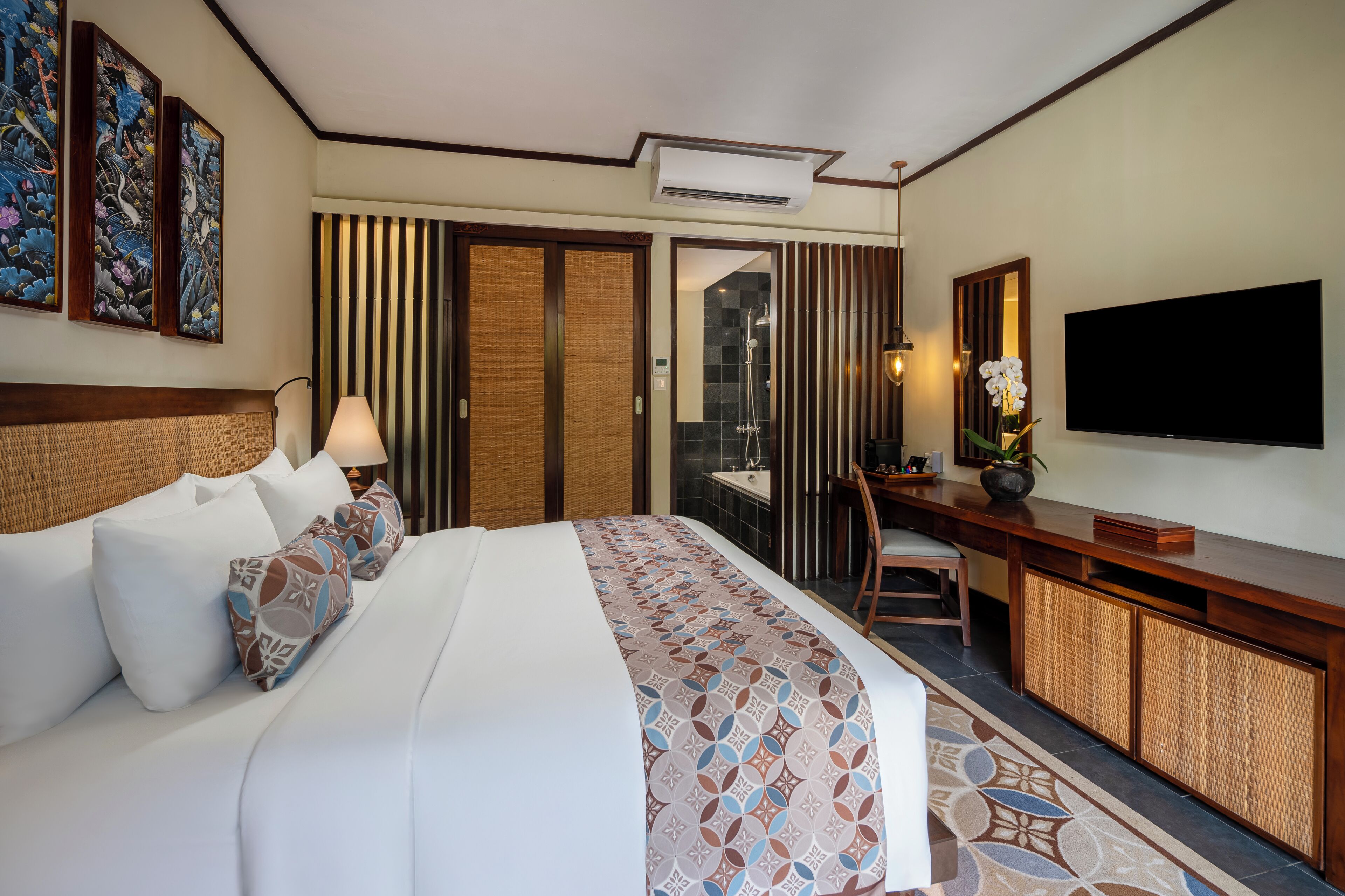 A hotel room with a large bed, a desk, a TV, and artwork on the walls.