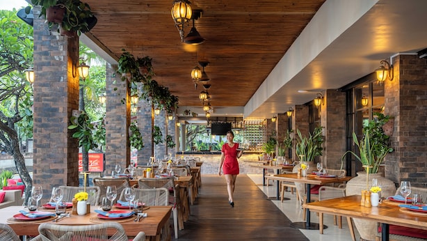 An indoor restaurant with wooden tables, wicker chairs, and hanging plants. - Kuta Seaview Beach Resort    (Kuta)