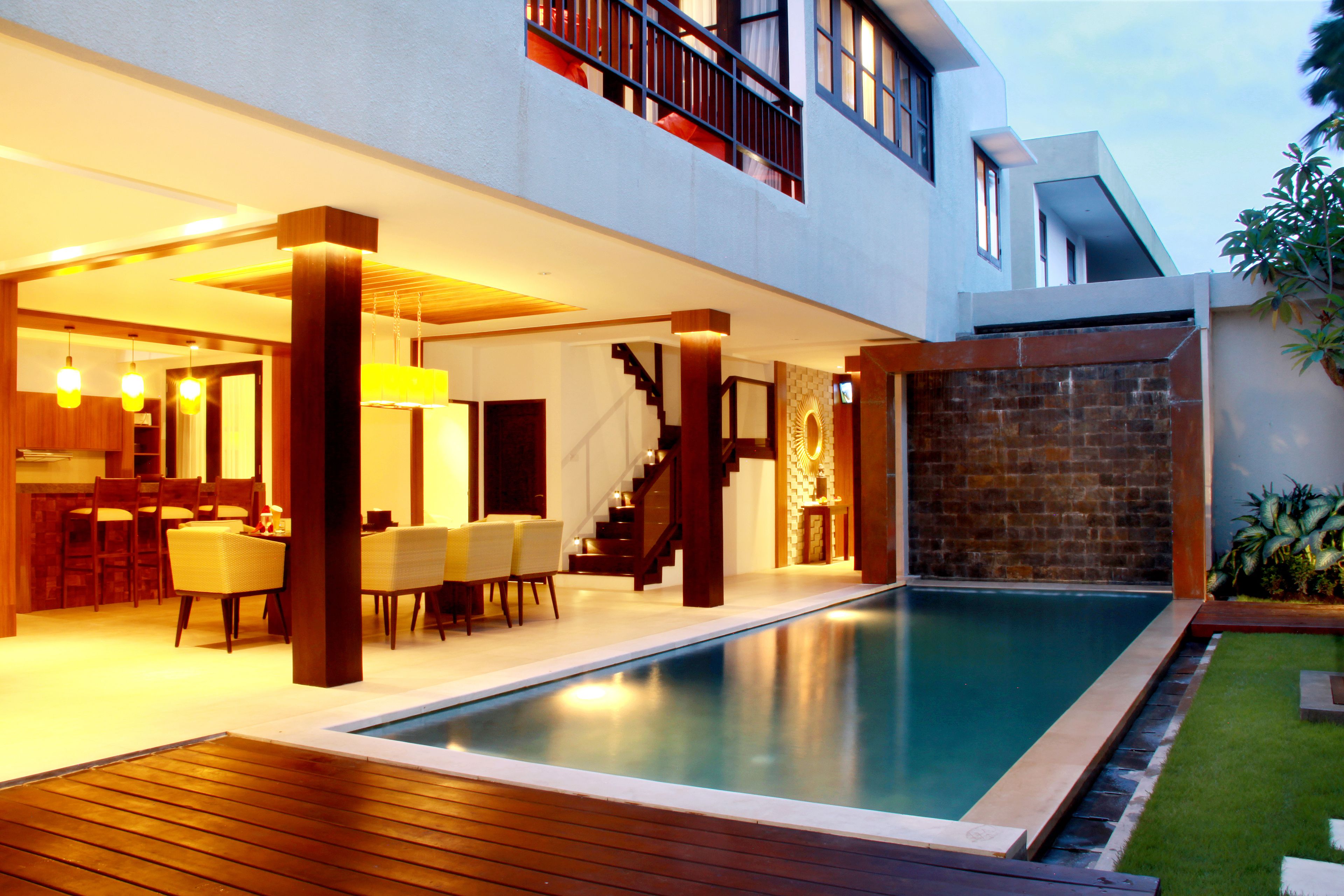 A modern house with a swimming pool, wooden deck, and a dining area with chairs and a table.
