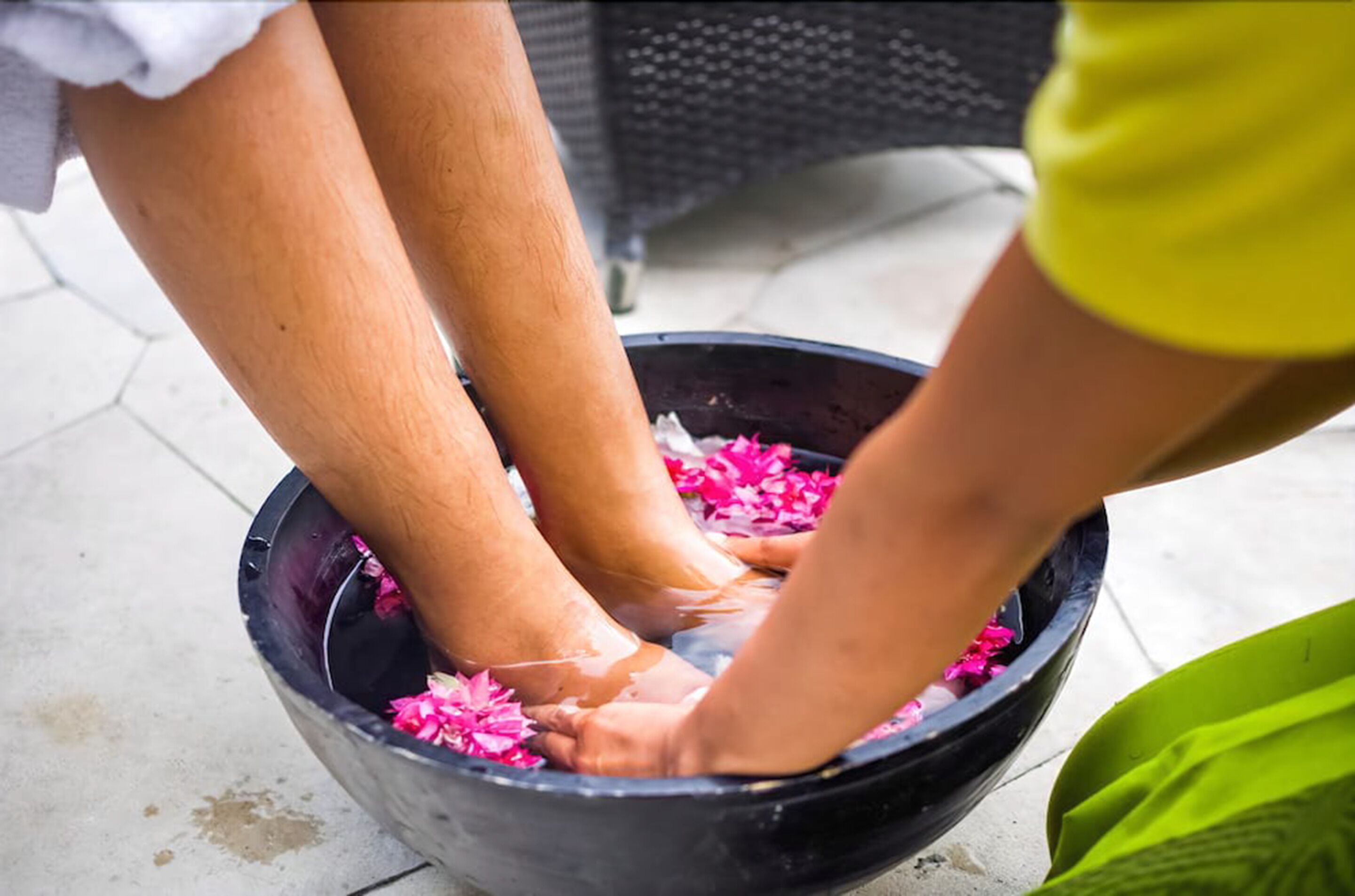 Una persona lava los pies en un recipiente negro lleno de agua y flores rosas.