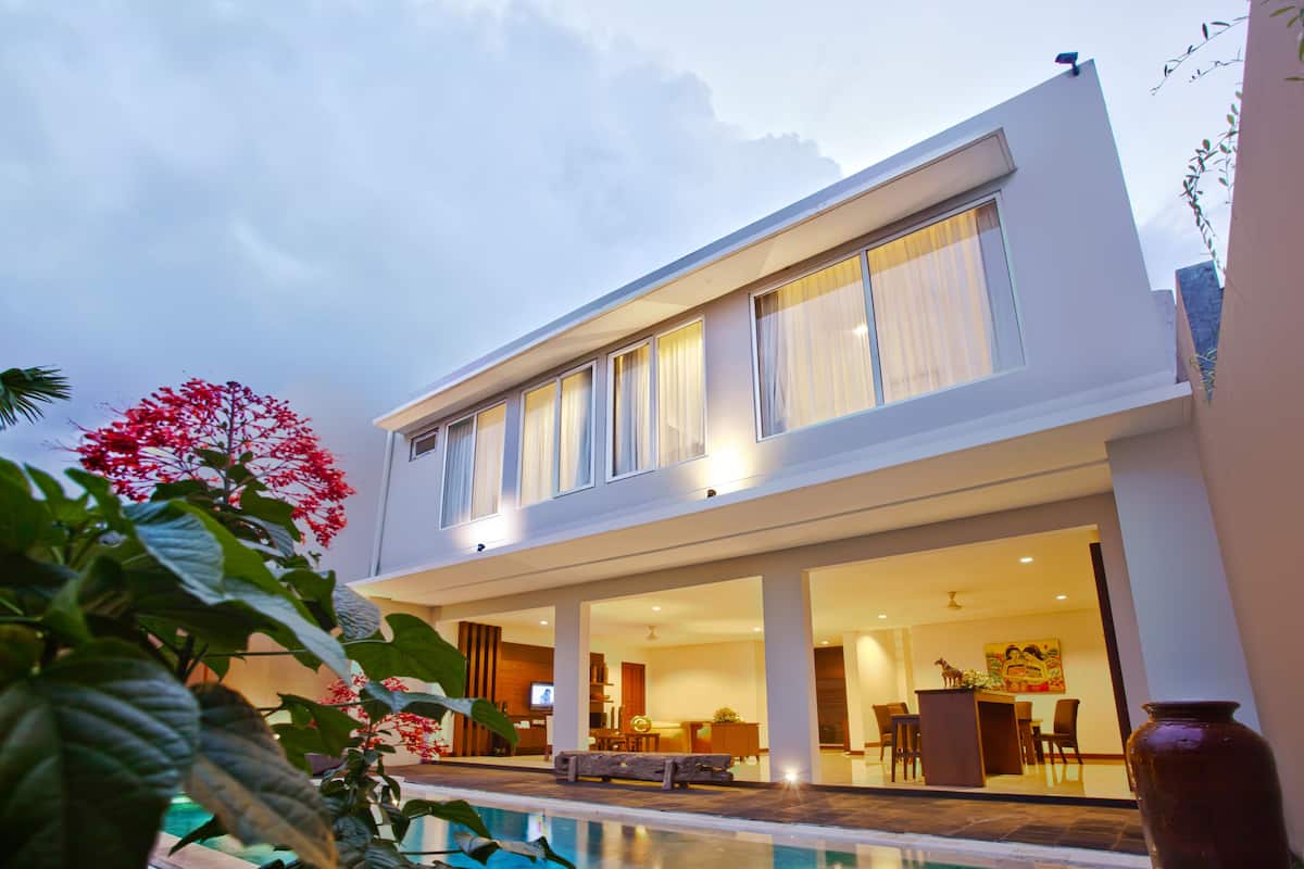 Une maison moderne à deux étages, dotée d’une piscine, de grandes fenêtres et d’un coin repas.