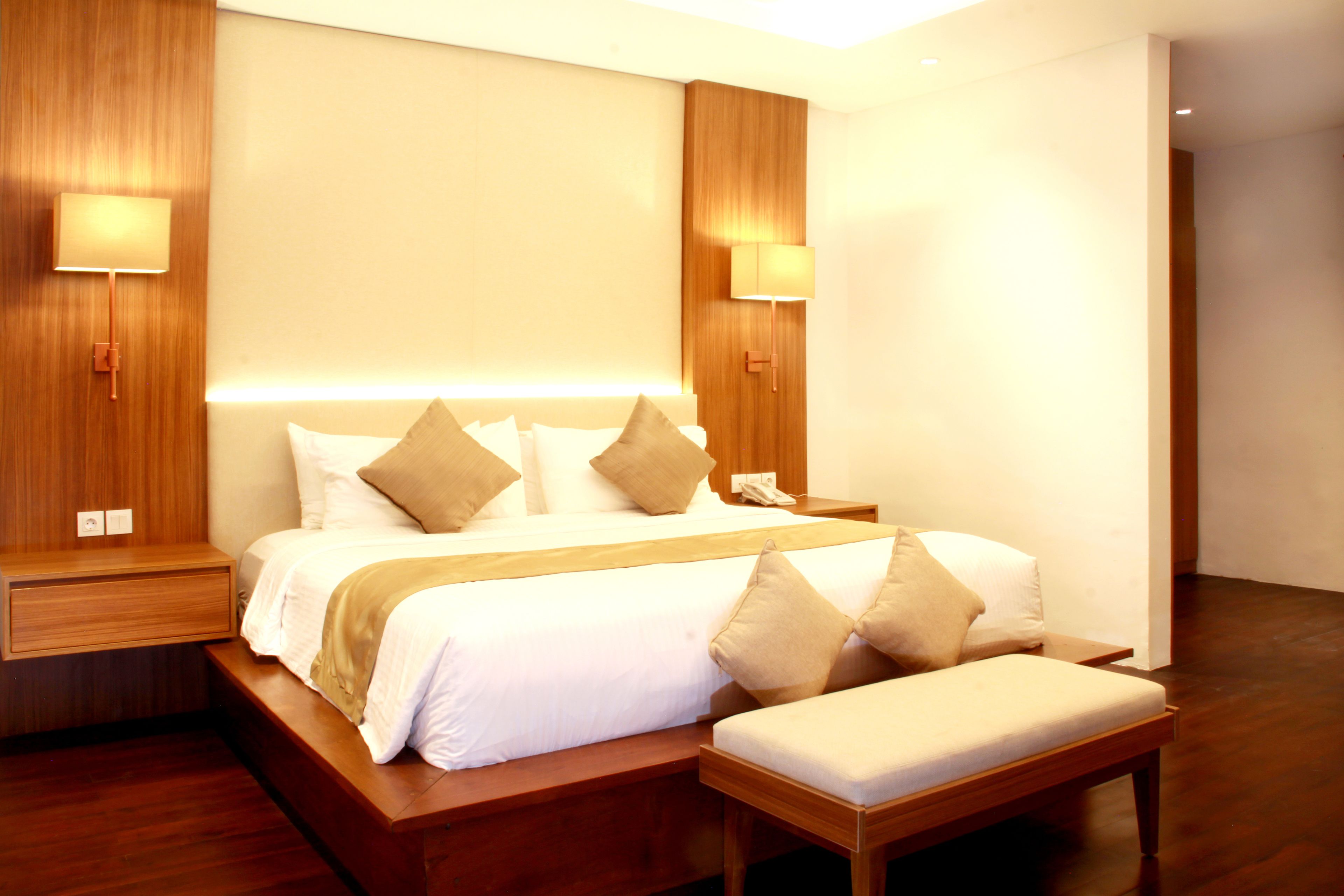 Une chambre d’hôtel moderne avec un grand lit, des tables de chevet et un banc.