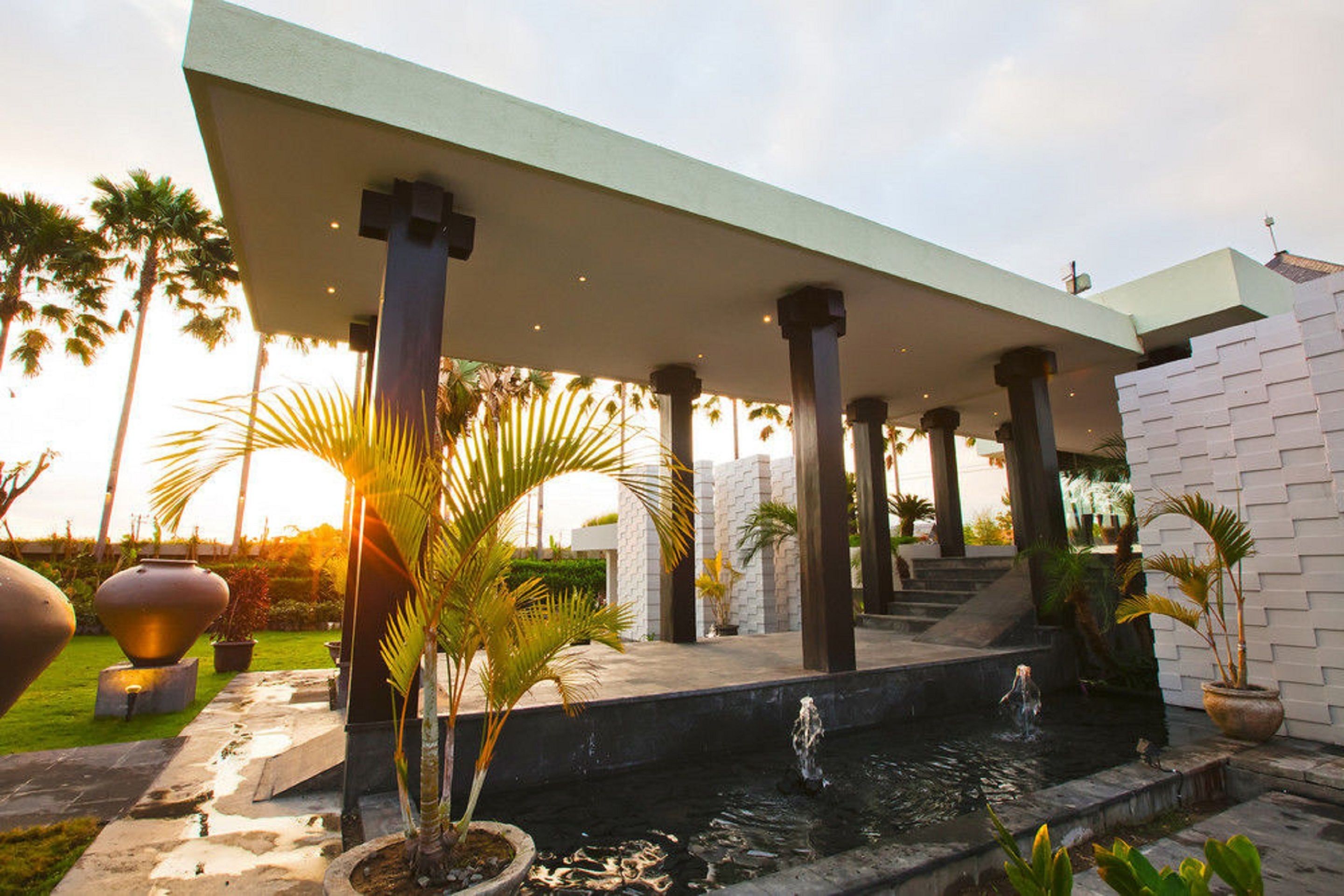 A covered outdoor area with a water feature, palm trees, and a brick wall.