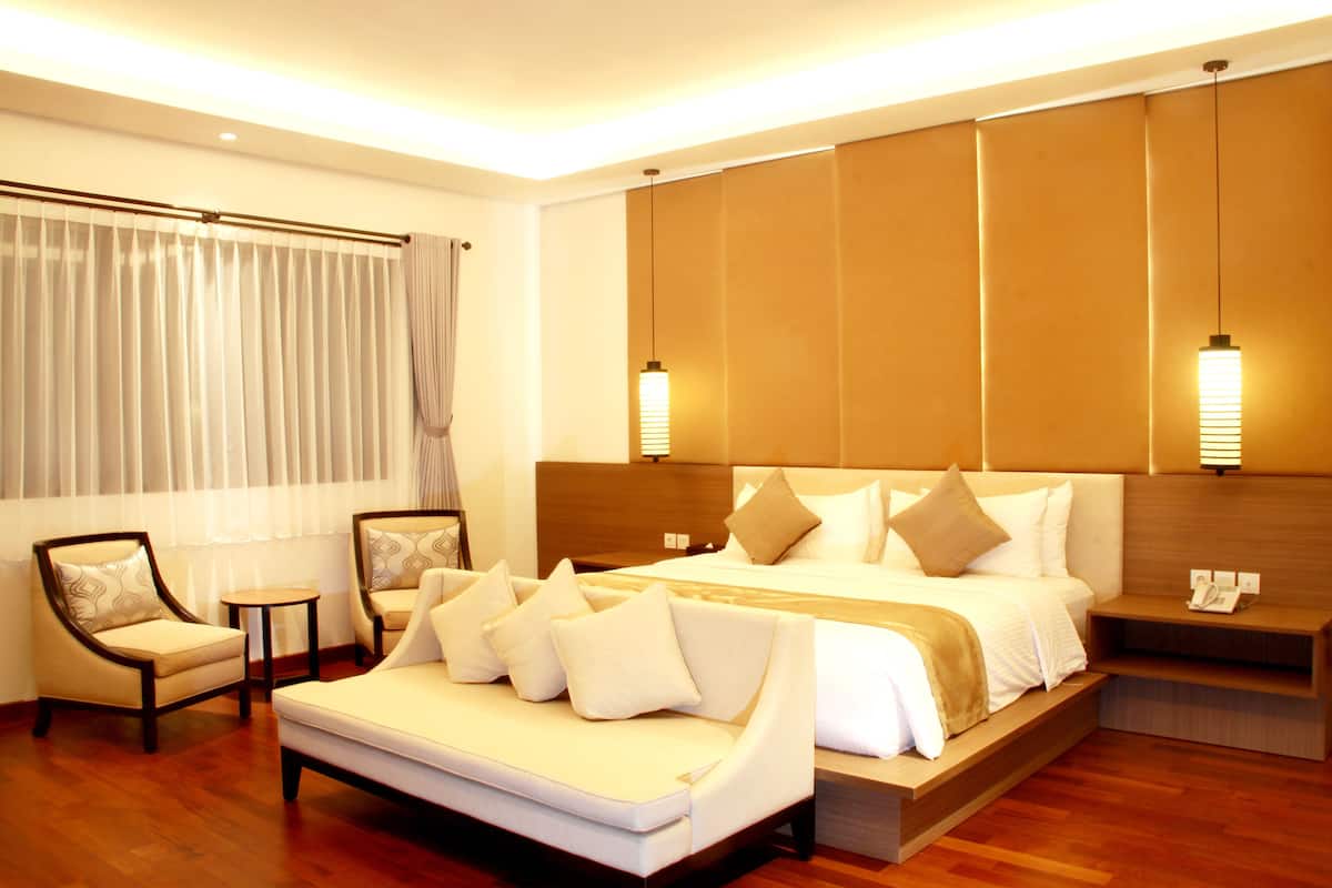 Une chambre d’hôtel avec un grand lit, un canapé, deux fauteuils, une petite table et une table de chevet avec un téléphone.