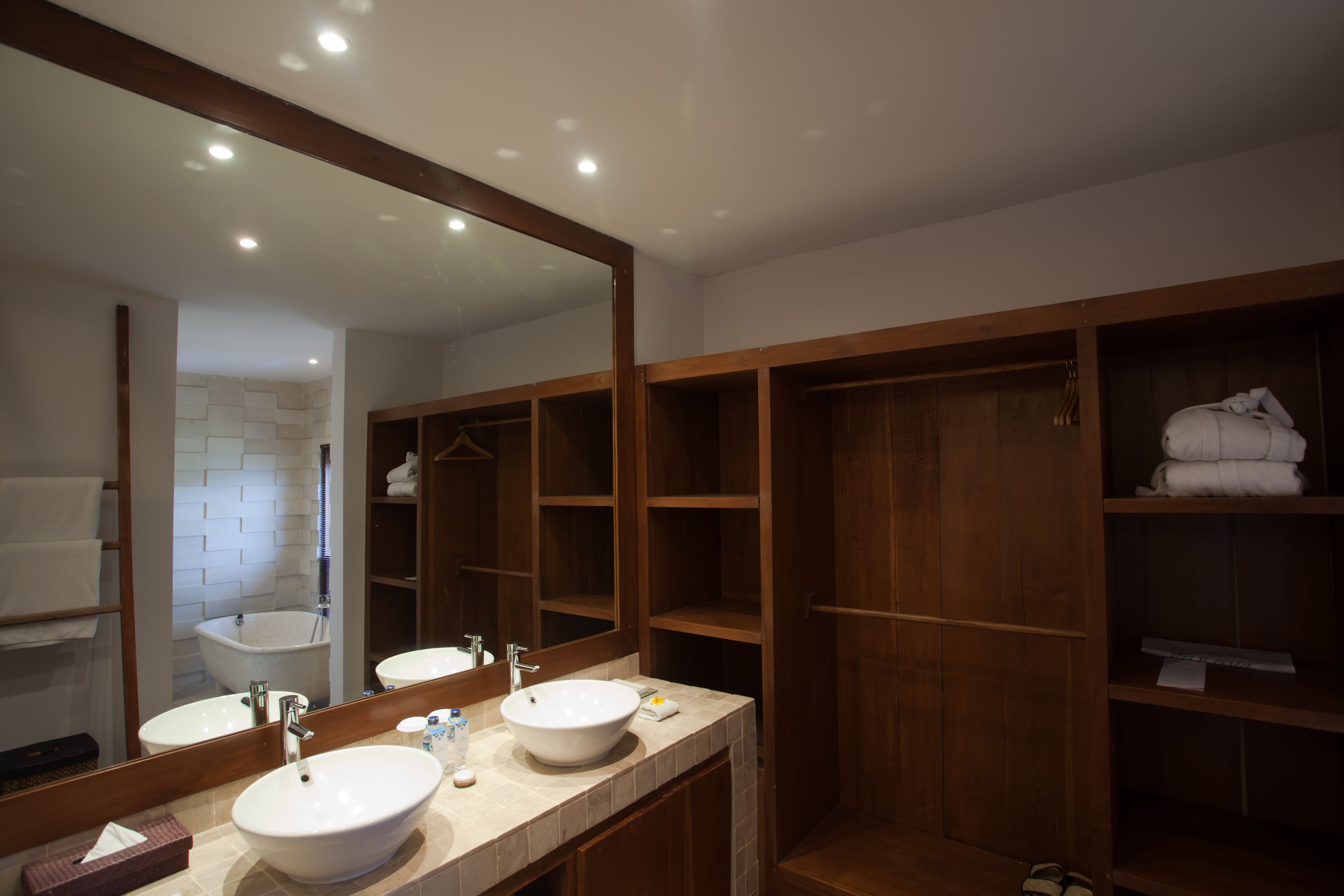 Un baño moderno con dos lavamanos, un espejo grande y estanterías de madera para toallas.