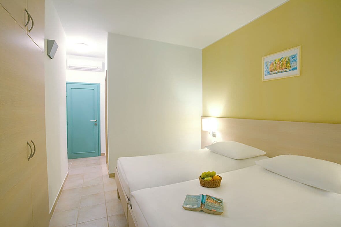 Quarto de hotel com duas camas, uma porta e um candeeiro fixo na parede.