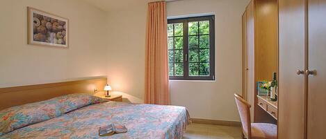 A bedroom with a bed, a desk, a chair, a window with curtains, and a wardrobe.