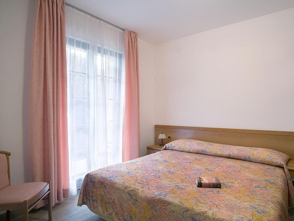 Ein Schlafzimmer mit Bett, Stuhl, Nachttisch und einem Fenster mit Vorhängen.