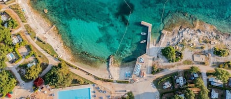 An aerial view of a coastal property with a swimming pool, RV parking, and clear turquoise waters.