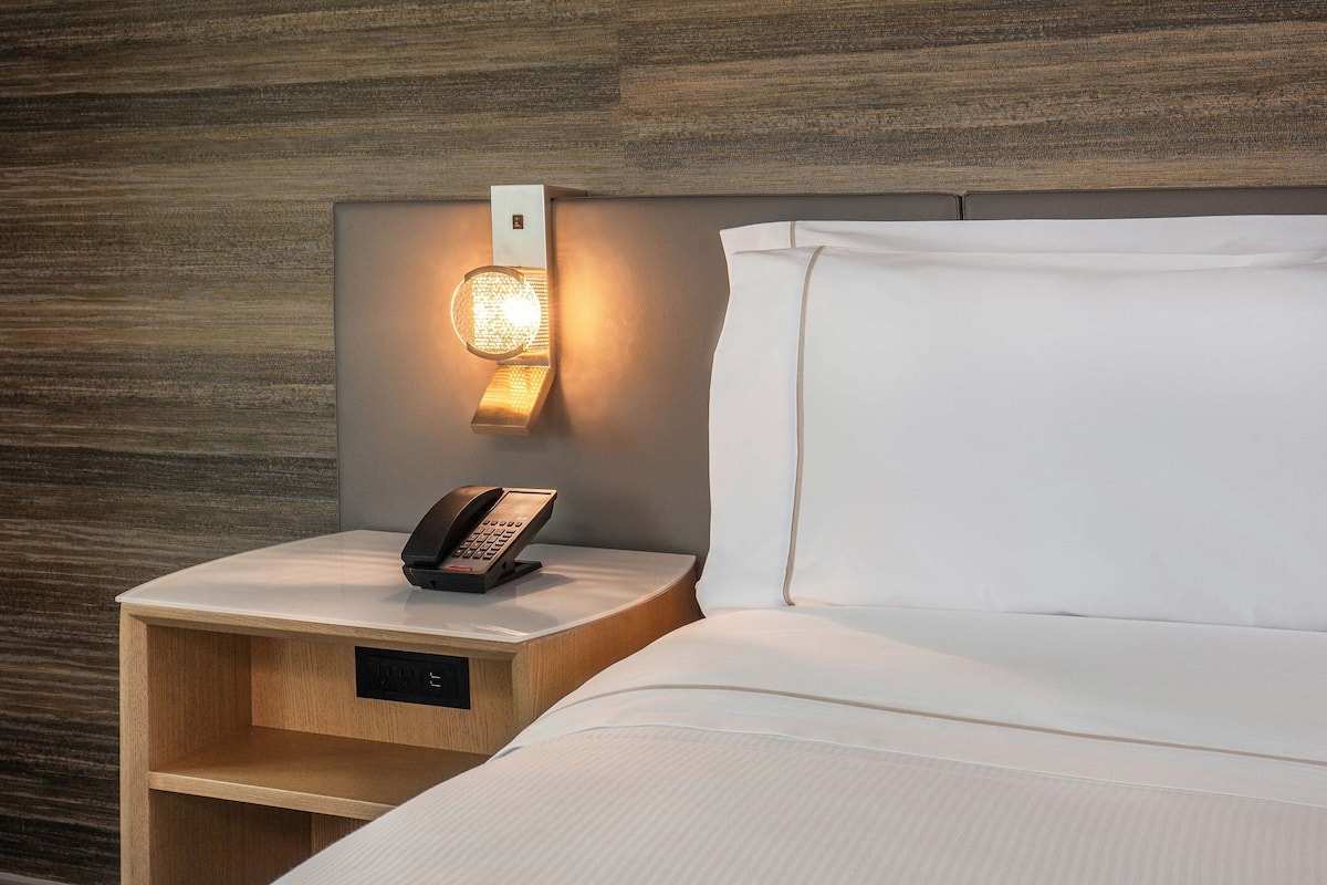 A hotel room with a wooden headboard, a bedside table with a phone, and a neatly made bed.