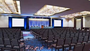 Un salón de conferencias con filas de sillas, una pantalla grande y un atril.