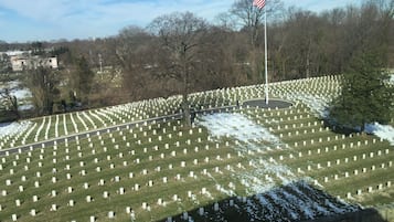 A cemetery with numerous white headstones arranged in rows, a flagpole with an American flag, and a stone wall in the foreground.
