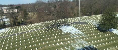Un cimetière avec de nombreuses pierres tombales blanches disposées en rangées, un mât portant le drapeau américain et un mur de pierre en premier plan.