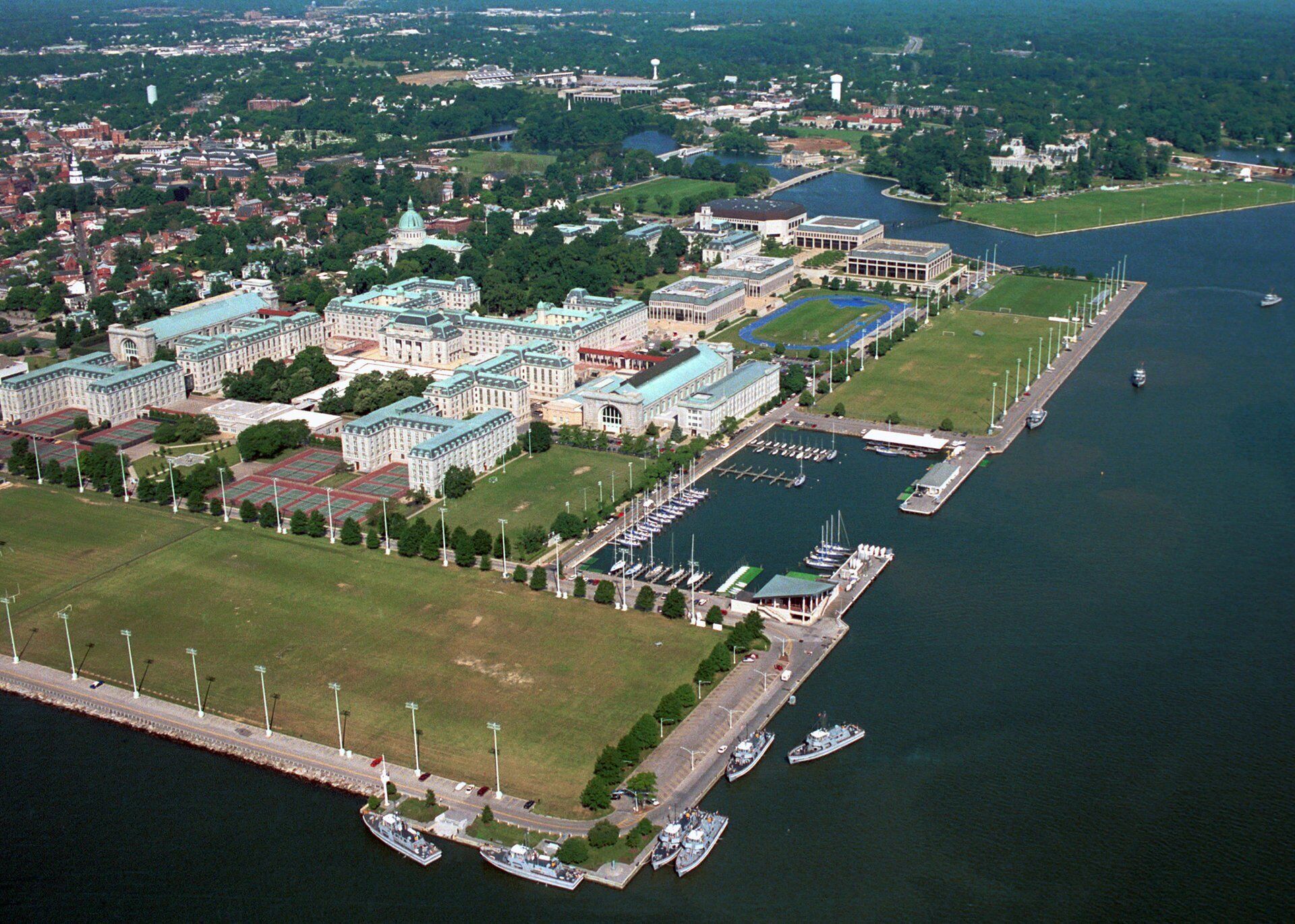 An aerial view of a large complex with multiple buildings, a marina with boats, and a river.