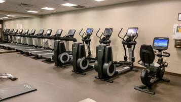 A row of stationary bikes in a gym with a clean, tiled floor and a plain wall.