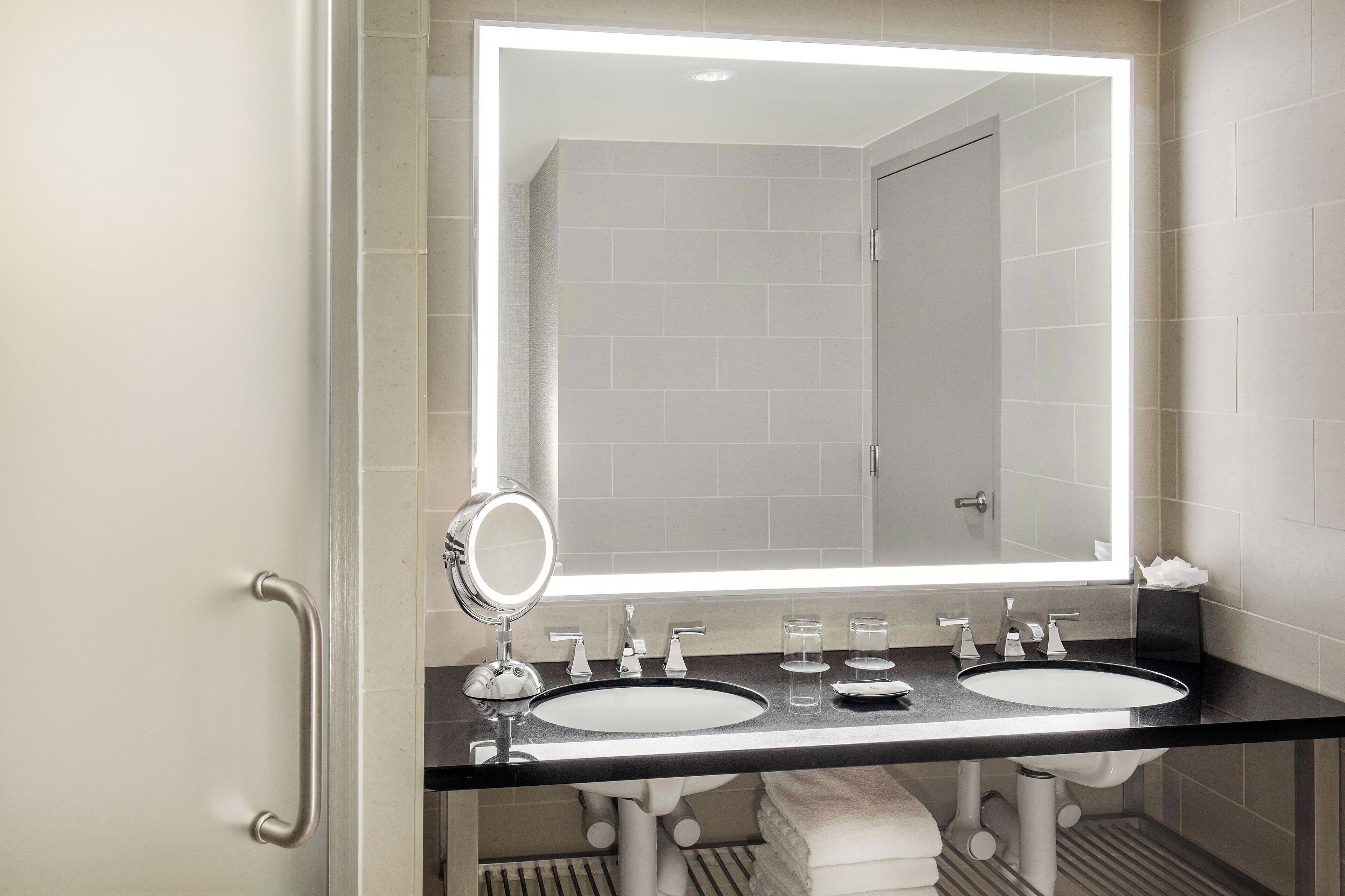 A modern bathroom with two sinks, a large mirror, and a vanity with a towel rack.