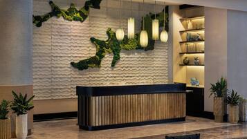 A reception area with a textured wall, a wooden reception desk, hanging pendant lights, and potted plants.