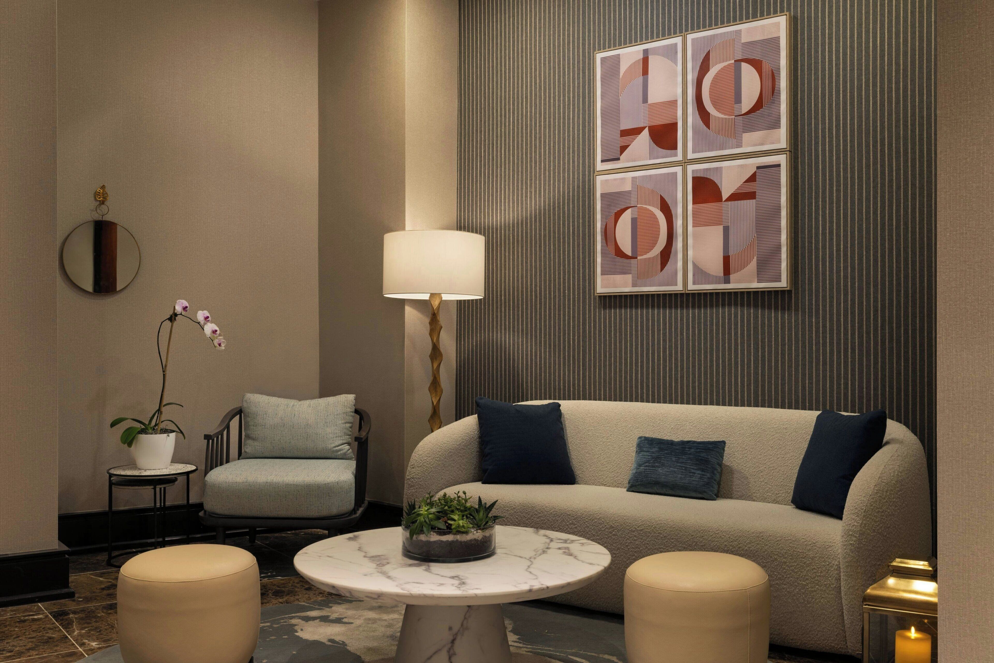A modern lounge area with a sofa, armchairs, a round table, a potted plant, and abstract wall art.